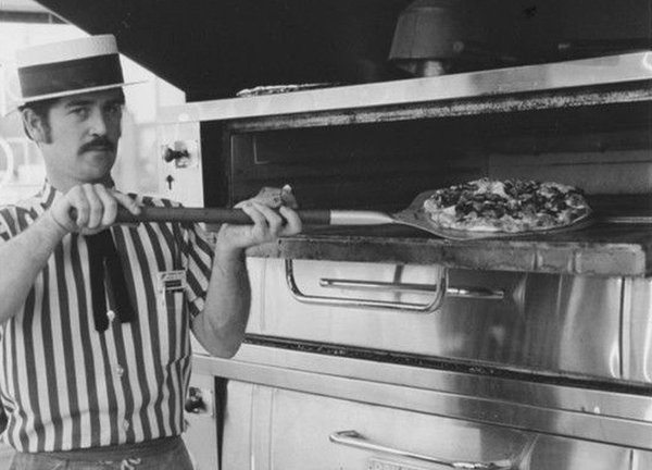 Old-tyme cook taking a pizza out of the oven